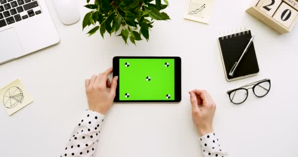 オフィスの机と緑色の画面と女性の手がそれをテーピングで黒いタブレット コンピューターの平面図です。水平。事務所の横にあるもの。クロマ キー。モーションのトラッキング — ストック動画