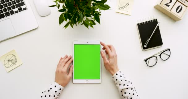 Vue de dessus sur le bureau et la tablette blanche avec écran vert et mains féminines collant dessus. Verticale. Des trucs de bureau à côté. Clé chromatique . — Video