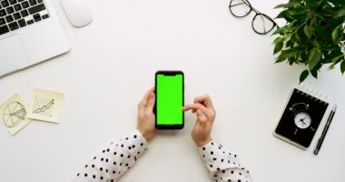 Üstten Görünüm Ofis Masası ve yeşil ekran ve üzerinde taping eller ile siyah smartphone. Dikey. Yanında başı işleri. Chroma anahtar.