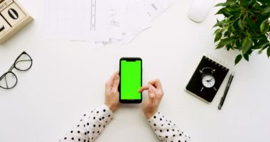 Üstten Görünüm Ofis Masası ve yeşil ekran ve üzerinde taping eller ile siyah smartphone. Dikey. Yanında başı işleri. Chroma anahtar.