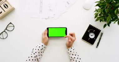 Üstten Görünüm Ofis Masası ve yeşil ekran ve üzerinde taping eller ile siyah smartphone. Yatay. Yanında başı işleri. Chroma anahtar.