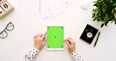 Üstten Görünüm Ofis Masası ve yeşil ekran ve eller üzerinde kayıt olan beyaz tablet bilgisayar. Dikey. Yanında başı işleri. Chroma anahtar. Hareket izleme