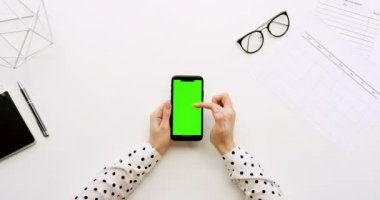 Üstten Görünüm Ofis Masası ve yeşil ekran ve üzerinde taping eller ile siyah smartphone. Dikey. Yanında başı işleri. Chroma anahtar.