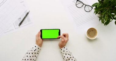 Üstten Görünüm Ofis Masası ve yeşil ekran ve üzerinde taping eller ile siyah smartphone. Yatay. Başı işleri ve kahve yanında. Chroma anahtar.