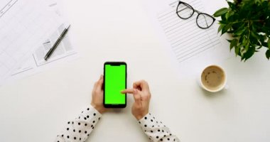 Üstten Görünüm Ofis Masası ve yeşil ekran ve üzerinde taping eller ile siyah smartphone. Dikey. Başı işleri ve kahve yanında. Chroma anahtar.