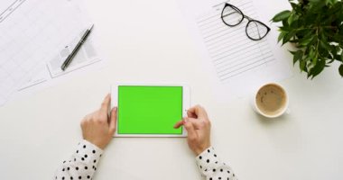 Üstten Görünüm Ofis Masası ve yeşil ekran ve eller üzerinde kayıt olan beyaz tablet bilgisayar. Yatay. Başı işleri ve kahve yanında. Chroma anahtar.