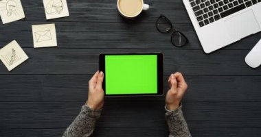 Üstten Görünüm siyah Ofis Masası ve yeşil ekran ve eller üzerinde kayıt olan siyah tablet bilgisayar. Yatay. Başı işleri, dizüstü bilgisayar ve kahve yanında. Chroma anahtar.