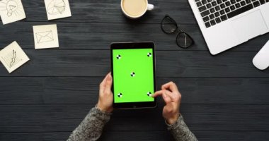 Üstten Görünüm siyah Ofis Masası ve yeşil ekran ve eller üzerinde kayıt olan siyah tablet bilgisayar. Dikey. Başı işleri, dizüstü bilgisayar ve kahve yanında. Chroma anahtar. Hareket izleme