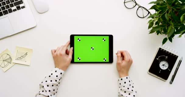 Vista superior na mesa de escritório e computador tablet preto com tela verde e as mãos femininas gravando sobre ele. Horizontal. Coisas de escritório ao lado. Chave Chroma. Movimento de rastreamento — Vídeo de Stock