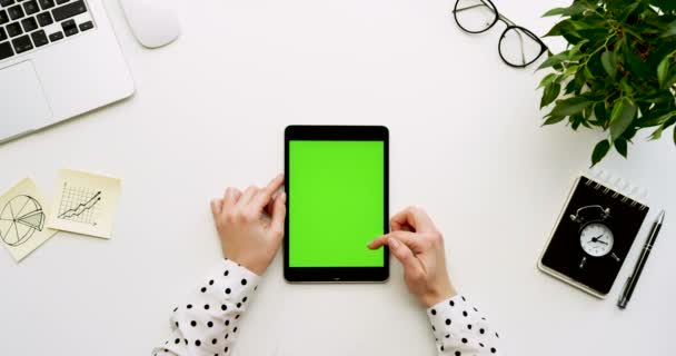 オフィスの机と緑色の画面と女性の手がそれをテーピングで黒いタブレット コンピューターの平面図です。垂直方向。事務所の横にあるもの。クロマ キー. — ストック動画