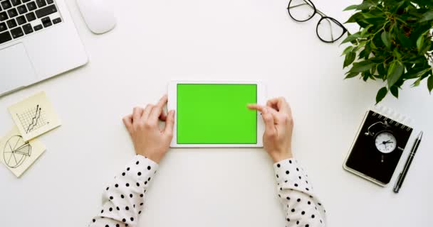 Vista superior na mesa de escritório e tablet branco com tela verde e as mãos femininas gravando sobre ele. Vertical. Coisas de escritório ao lado. Chave Chroma . — Vídeo de Stock