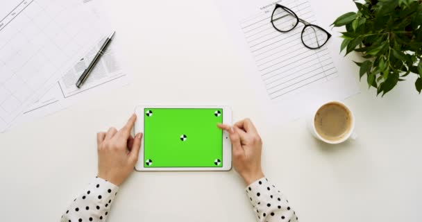 オフィスの机と緑色の画面と女性の手がそれをテーピングで白いタブレット コンピューターの平面図です。水平。事務所スタッフとコーヒーの横にあります。クロマ キー。モーションのトラッキング. — ストック動画