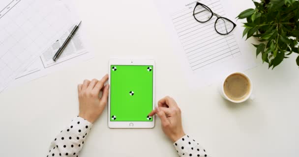 オフィスの机と緑色の画面と女性の手がそれをテーピングで白いタブレット コンピューターの平面図です。垂直方向に。事務所スタッフとコーヒーの横にあります。クロマ キー。モーションのトラッキング. — ストック動画