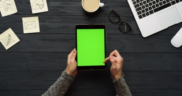 Ovanifrån på svart skrivbord och svart surfplatta med grön skärm och kvinnliga händer tejpa på den. Lodrät. Kontor grejer, laptop och kaffe bredvid. Färgtransparens. — Stockvideo