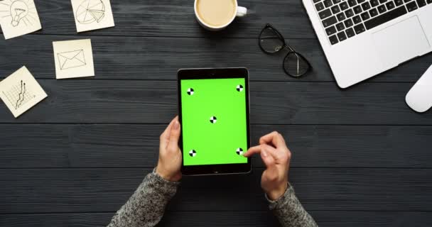 Vista dall'alto sulla scrivania dell'ufficio nero e computer tablet nero con schermo verde e le mani femminili su di esso. Verticale. Roba da ufficio, laptop e caffe 'accanto. Chiave cromatica. Movimento di tracciamento — Video Stock