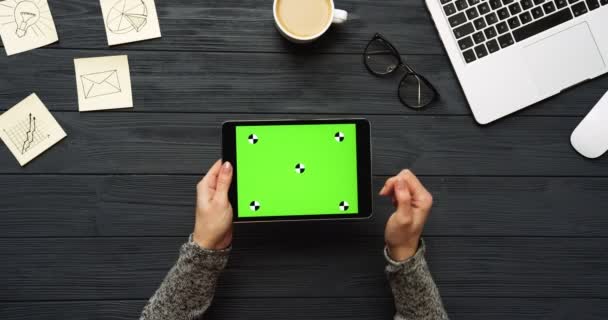 Vista dall'alto sulla scrivania dell'ufficio nero e computer tablet nero con schermo verde e le mani femminili su di esso. Orizzontale. Roba da ufficio, laptop e caffe 'accanto. Chiave cromatica. Movimento di tracciamento — Video Stock