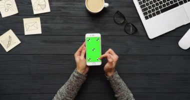Üstten Görünüm siyah Ofis Masası ve beyaz Smartphone ile yeşil perde ve eller üzerinde kayıt. Dikey. Başı işleri, dizüstü bilgisayar ve kahve yanında. Chroma anahtar. Hareket izleme