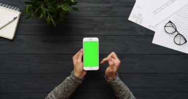 Üstten Görünüm siyah Ofis Masası ve beyaz Smartphone ile yeşil perde ve eller üzerinde kayıt. Dikey. Yanında başı işleri. Chroma anahtar.