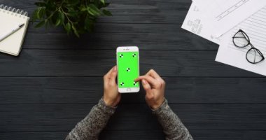 Üstten Görünüm siyah Ofis Masası ve beyaz Smartphone ile yeşil perde ve eller üzerinde kayıt. Dikey. Yanında başı işleri. Chroma anahtar. Hareket izleme