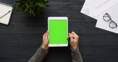 Üstten Görünüm siyah Ofis Masası ve yeşil ekran ve eller üzerinde kayıt olan beyaz tablet bilgisayar. Dikey. Yanında başı işleri. Chroma anahtar.