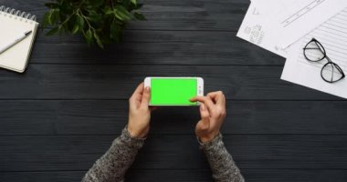 Üstten Görünüm siyah Ofis Masası ve beyaz Smartphone ile yeşil perde ve eller üzerinde kayıt. Yatay. Yanında başı işleri. Chroma anahtar.