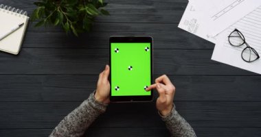 Üstten Görünüm siyah Ofis Masası ve yeşil ekran ve eller üzerinde kayıt olan siyah tablet bilgisayar. Dikey. Yanında başı işleri. Chroma anahtar. Hareket izleme