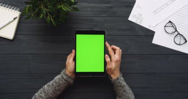 Üstten Görünüm siyah Ofis Masası ve yeşil ekran ve eller üzerinde kayıt olan siyah tablet bilgisayar. Dikey. Yanında başı işleri. Chroma anahtar.