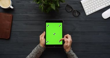 Üstten Görünüm siyah Ofis Masası ve yeşil ekran ve eller üzerinde kayıt olan siyah tablet bilgisayar. Dikey. Yanında başı işleri. Chroma anahtar. Hareket izleme