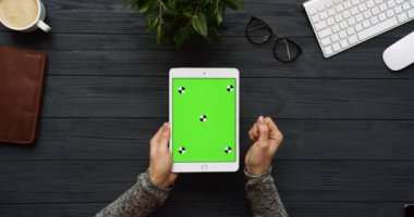 Üstten Görünüm siyah Ofis Masası ve yeşil ekran ve eller üzerinde kayıt olan beyaz tablet bilgisayar. Dikey. Yanında başı işleri. Chroma anahtar. Hareket izleme