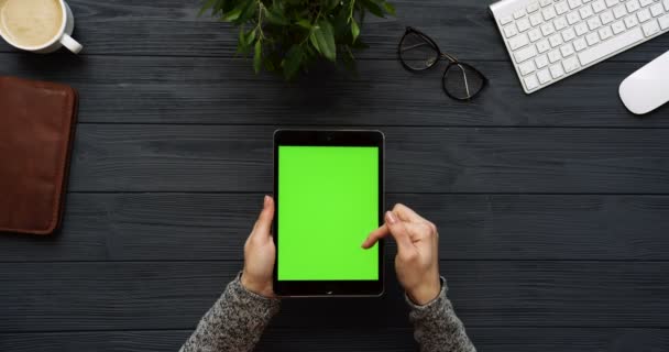 Vista superior en el escritorio negro de la oficina y la tableta negra con la pantalla verde y las manos femeninas pegadas en ella. Vertical. Cosas de oficina al lado. Clave de croma . — Vídeo de stock