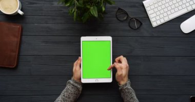 Üstten Görünüm siyah Ofis Masası ve yeşil ekran ve eller üzerinde kayıt olan beyaz tablet bilgisayar. Dikey. Yanında başı işleri. Chroma anahtar.