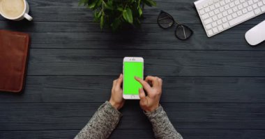 Üstten Görünüm siyah Ofis Masası ve beyaz Smartphone ile yeşil perde ve eller üzerinde kayıt. Dikey. Yanında başı işleri. Chroma anahtar.