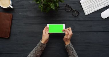 Üstten Görünüm siyah Ofis Masası ve beyaz Smartphone ile yeşil perde ve eller üzerinde kayıt. Yatay. Yanında başı işleri. Chroma anahtar.