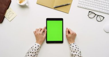 Üstten Görünüm beyaz Ofis Masası ve yeşil ekran ve eller üzerinde kayıt olan siyah tablet bilgisayar. Dikey. Yanında başı işleri. Chroma anahtar.