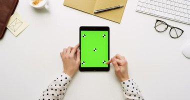 Üstten Görünüm beyaz Ofis Masası ve yeşil ekran ve eller üzerinde kayıt olan siyah tablet bilgisayar. Dikey. Yanında başı işleri. Chroma anahtar. Hareket izleme