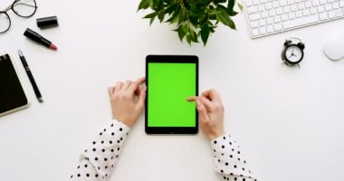Üstten Görünüm beyaz Ofis Masası ve yeşil ekran ve eller üzerinde kayıt olan siyah tablet bilgisayar. Dikey. Yanında başı işleri. Chroma anahtar.