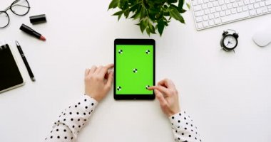 Üstten Görünüm beyaz Ofis Masası ve yeşil ekran ve eller üzerinde kayıt olan siyah tablet bilgisayar. Dikey. Yanında başı işleri. Chroma anahtar. Hareket izleme