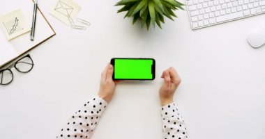 Üstten Görünüm beyaz Ofis Masası ve yeşil ekran ve üzerinde taping eller ile siyah smartphone. Yatay. Yanında başı işleri. Chroma anahtar.