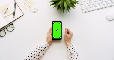 Üstten Görünüm beyaz Ofis Masası ve yeşil ekran ve üzerinde taping eller ile siyah smartphone. Dikey. Yanında başı işleri. Chroma anahtar. Hareket izleme