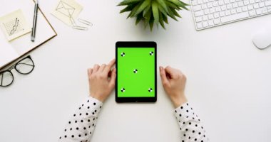 Üstten Görünüm beyaz Ofis Masası ve yeşil ekran ve eller üzerinde kayıt olan siyah tablet bilgisayar. Dikey. Yanında başı işleri. Chroma anahtar. Hareket izleme