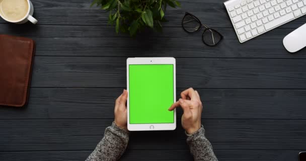 Ovanifrån på svart skrivbord och vit tablett dator med grön skärm och kvinnliga händer tejpa på den. Lodrät. Kontor grejer bredvid. Färgtransparens. — Stockvideo