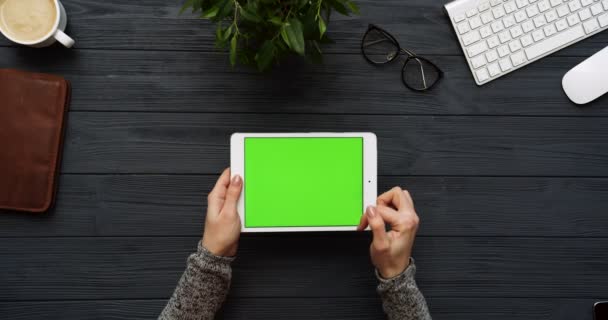 Vista superior en el escritorio de oficina negro y tableta blanca con pantalla verde y manos femeninas pegadas en ella. Horizontal. Cosas de oficina al lado. Clave de croma . — Vídeo de stock