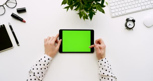 Vue de dessus sur le bureau blanc et la tablette noire avec écran vert et mains féminines collant dessus. Horizontal. Des trucs de bureau à côté. Clé chromatique . — Video
