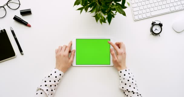 Bovenaanzicht op de witte Bureau en witte tabletcomputer met groen scherm en vrouwelijke handen taping daarop. Horizontaal. Kantoor spullen naast. Chromakey. — Stockvideo