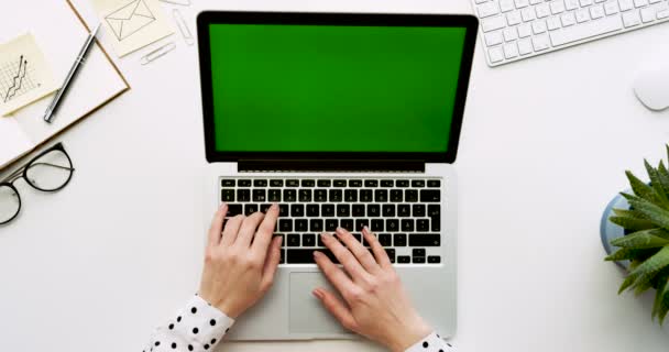 Vista superior na mesa de escritório com computador portátil com tela verde e as mãos femininas gravando sobre ele. Coisas de escritório ao lado. Chave Chroma . — Vídeo de Stock