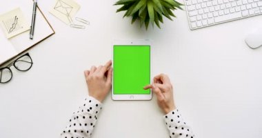 Üstten Görünüm beyaz Ofis Masası ve yeşil ekran ve eller üzerinde kayıt olan beyaz tablet bilgisayar. Dikey. Yanında başı işleri. Chroma anahtar.