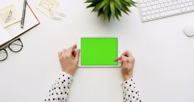 Üstten Görünüm beyaz Ofis Masası ve yeşil ekran ve eller üzerinde kayıt olan beyaz tablet bilgisayar. Yatay. Yanında başı işleri. Chroma anahtar.