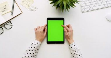 Üstten Görünüm beyaz Ofis Masası ve yeşil ekran ve eller üzerinde kayıt olan siyah tablet bilgisayar. Dikey. Yanında başı işleri. Chroma anahtar.