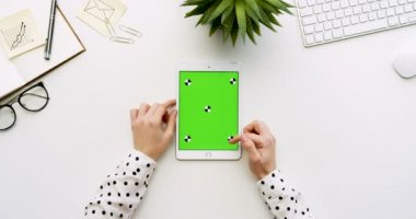Üstten Görünüm beyaz Ofis Masası ve yeşil ekran ve eller üzerinde kayıt olan beyaz tablet bilgisayar. Dikey. Yanında başı işleri. Chroma anahtar. Hareket izleme