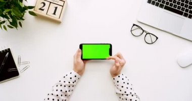 Üstten Görünüm beyaz Ofis Masası ve yeşil ekran ve üzerinde taping eller ile siyah smartphone. Yatay. Başı işleri, dizüstü bilgisayar ve gözlük yanında. Chroma anahtar.
